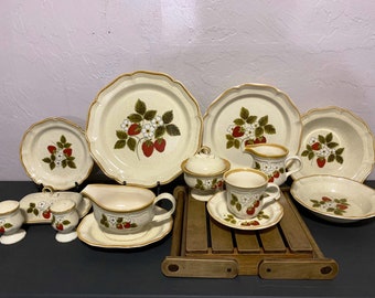 May include: A set of vintage strawberry patterned stoneware dinnerware. The set includes a large platter, a smaller platter, two bowls, a creamer, a sugar bowl, a gravy boat, a cup and saucer, and two salt and pepper shakers.