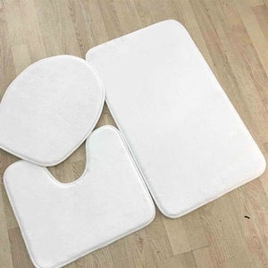 Puede incluir: Un juego de tres alfombras de baño blancas. El juego incluye una alfombra de baño, una tapa de asiento de inodoro y una alfombra de contorno.