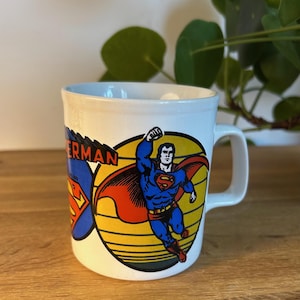 Peut inclure: Une tasse en céramique blanche avec un motif Superman. La tasse présente un logo Superman rouge, jaune et bleu avec le texte "Superman" sur le côté.
