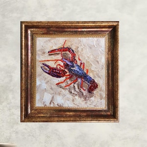 May include: Square framed painting of a lobster. The lobster is painted in shades of red and blue, with a textured, off-white background. The frame is a dark gold color.