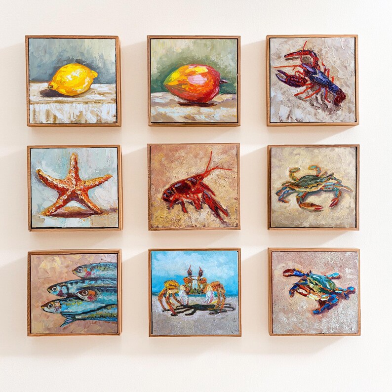 May include: Nine square framed paintings with wooden frames. The paintings depict various subjects, including a lemon, a mango, a lobster, a starfish, a crawfish, a crab, a group of fish, crabs on a beach, and a crab.