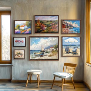 May include: A collection of framed landscape and seascape paintings. The artwork includes scenes of a white house in a field of purple flowers, coastal views, and beach scenes with sailboats and chairs. The paintings are in brown frames and hang on a gray wall.