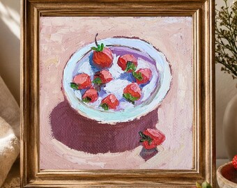 May include: An oil painting in a gold frame depicting a white bowl filled with red strawberries and white cream. The bowl sits on a light pink surface, casting a dark purple shadow. One additional strawberry rests on the surface outside the bowl.