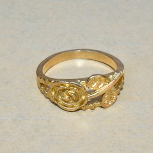 Könnte beinhalten: Ein goldener Ring mit Rosenmotiv. Der Ring ist aus Metall und hat eine glatte Oberfläche.
