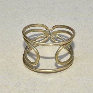Puede incluir: Un brazalete de metal dorado con un diseño geométrico simple. El brazalete está hecho de dos bandas de metal superpuestas que crean un look único y elegante.