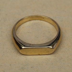 Può includere: Un anello a sigillo in oro con una parte superiore piatta e rettangolare.