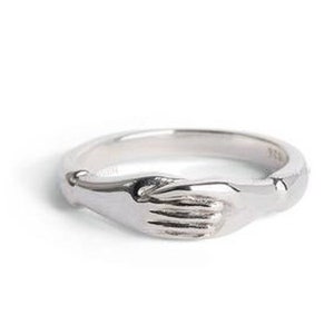 May include: A silver ring with two hands clasped together, forming a circle.