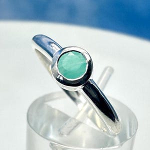 Könnte beinhalten: Ein silberner Ring mit einem runden, hellgrünen Edelstein, der in einer Zargenfassung sitzt.