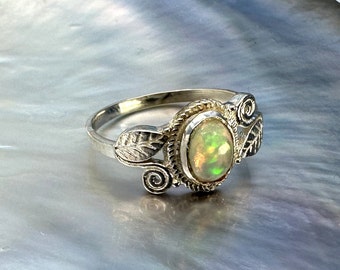 Puede incluir: Un anillo de plata con una piedra de ópalo ovalada engastada en un diseño de hojas y espirales.