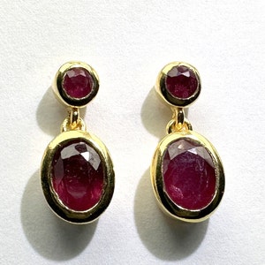 Op de afbeelding: Een paar gouden oorbellen met elk twee robijnstenen. De bovenste steen is rond en de onderste steen is ovaal.