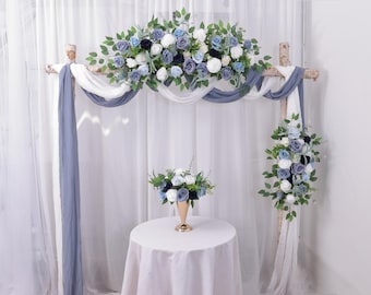 May include: A wedding arch decorated with blue and white silk flowers. The arch is made of wood and is draped with white and blue fabric. A small bouquet of blue and white flowers sits on a white table in front of the arch.