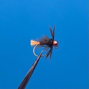Peut inclure: Une mouche de pêche à la mouche noire et verte avec une queue orange et une tête de perle de cuivre.