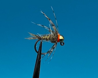 May include: A gold-colored fly fishing lure with a red and orange band around the head. The lure has a brown and black body with a variety of feathers and fibers.