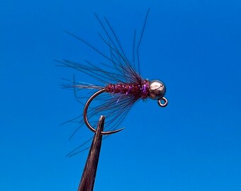May include: A purple and silver fly fishing lure with a feathered tail and a bead head.