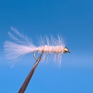 Könnte beinhalten: Ein weißer Fliegenfischköder mit einem goldenen Perlenkopf und einem weißen Federschwanz.