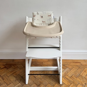 A high chair with a cream full cover silicone place mat on the attached tray. Includes a dog illustrated white cushion in the seat