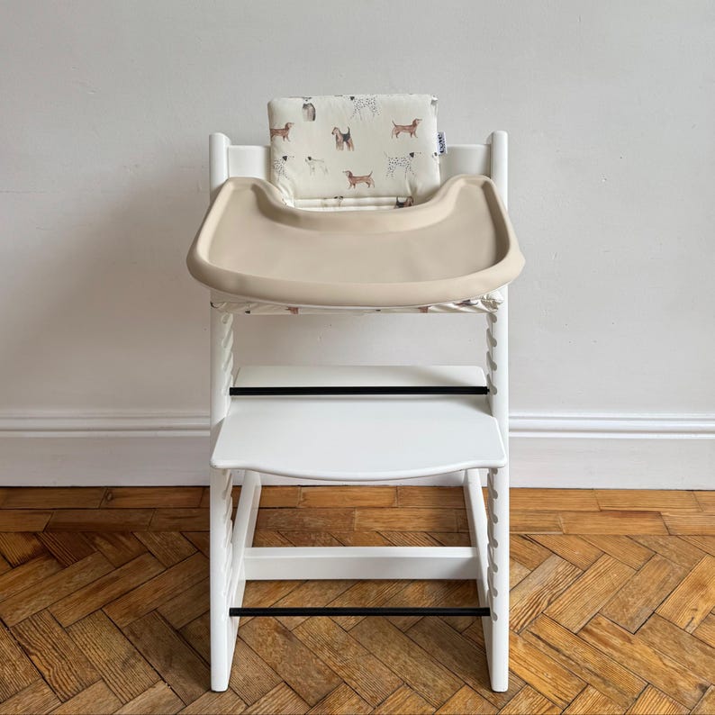 A high chair with a cream full cover silicone place mat on the attached tray. Includes a dog illustrated white cushion in the seat