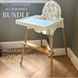 Puede incluir: Una trona blanca con una bandeja azul claro y una funda de cojín estampada. La trona tiene patas de madera y un reposapiés. El texto de la imagen dice: "FULL HIGHCHAIR ACCESSORIES BUNDLE" y "INCLUDES: CUSHION COVER, PLACEMAT, LEG WRAPS, FOOTREST."