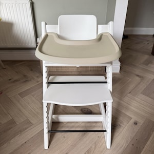 A high chair with a cream full cover silicone place mat on the attached tray.
