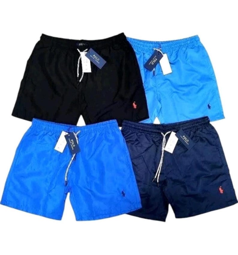 May include: Four pairs of swim trunks in black, light blue, and navy blue. Each pair has a drawstring, a small red logo, and a tag. The trunks are made of a smooth, shiny material.