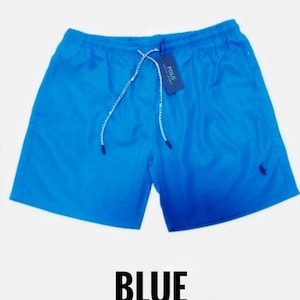 May include: Bright blue swim shorts with a drawstring waist and a small logo on the leg. The shorts have a tag attached. The word "BLUE" is printed in large, bold letters at the bottom of the image.