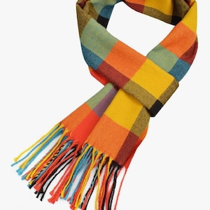 May include: A vibrant scarf featuring a plaid design in yellow, orange, red, blue, and black. The scarf has fringed edges with strands of different colours. The scarf is made of a soft material, ideal for cooler weather.