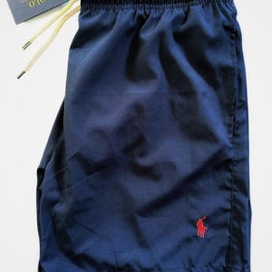 May include: Navy blue shorts with an elastic waistband and drawstring. A small red polo player logo is on the lower left leg. The shorts have a tag that reads "POLO RALPH LAUREN". The word "NAVY" is printed at the bottom.