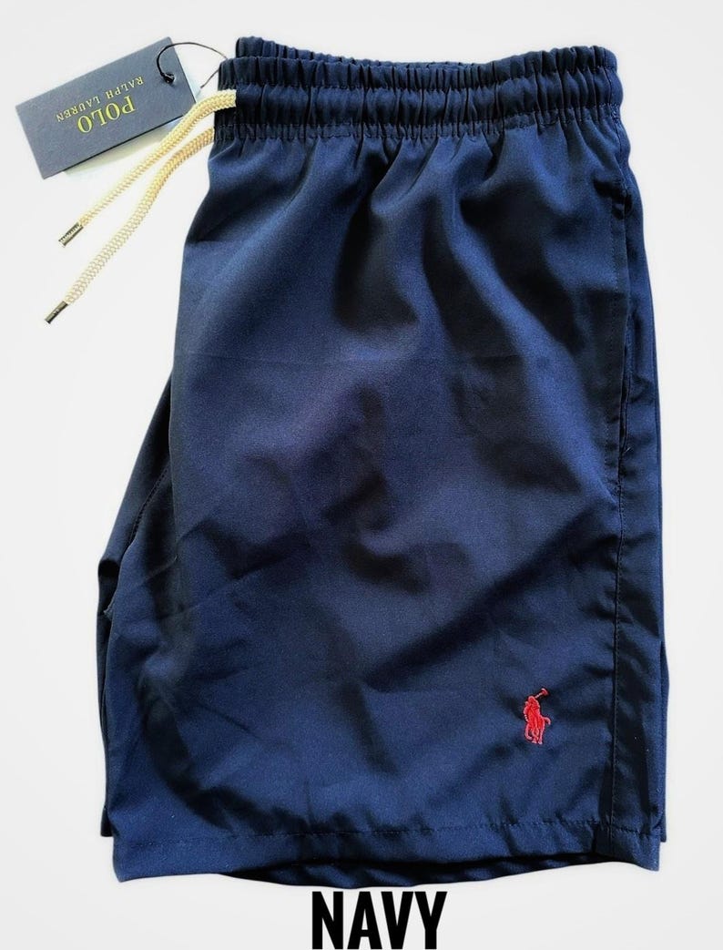 May include: Navy blue shorts with an elastic waistband and drawstring. A small red polo player logo is on the lower left leg. The shorts have a tag that reads "POLO RALPH LAUREN". The word "NAVY" is printed at the bottom.