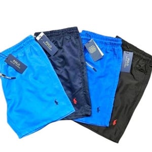 May include: Four pairs of men's swim trunks in various colors: light blue, navy, bright blue, and black. Each pair features a drawstring waist, a small logo, and a tag that reads "POLO".