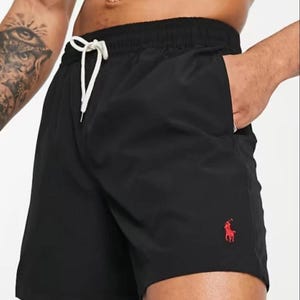 May include: Black swim shorts with a drawstring waist and a red logo on the leg. The shorts have a relaxed fit and pockets. Perfect for a day at the beach or pool.
