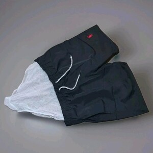 May include: Black swim trunks with a white mesh lining. The trunks have a drawstring closure with white cords and a small red logo on the upper left side. The shorts are made of a lightweight, water-resistant material.