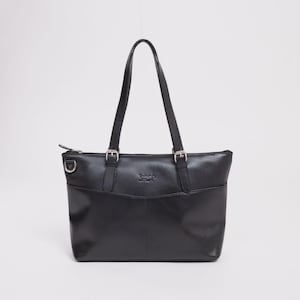 Pode incluir: Uma bolsa tote de couro preta com duas alças superiores e fivelas prateadas. A bolsa tem formato retangular com um bolso frontal e fecho de zíper. A bolsa é projetada para transportar itens.