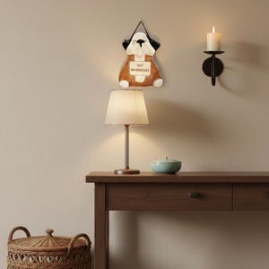 Può includere: Un'applique a forma di cane con la scritta "NO WHINING". Una candela accesa in un'applique nera è montata sulla parete. Una lampada da tavolo e una piccola ciotola blu sono su un tavolo di legno. Un cesto di vimini è sul pavimento.