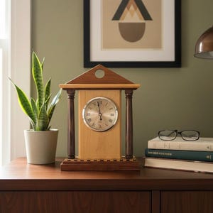 Op de afbeelding: Een houten mantelklok met een lichtgekleurde wijzerplaat en Romeinse cijfers. De klok heeft donkerbruine zuilen en een driehoekige top. Hij staat op een donkerhouten oppervlak, naast een potplant en boeken. Een ingelijst abstract kunstwerk hangt op de achtergrond.