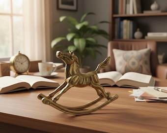 Puede incluir: Una figura de caballo balancín dorada sobre un escritorio de madera. El caballo está detallado con crin, cola y silla. Otros elementos en el escritorio incluyen un libro abierto, un reloj, una taza y una planta.