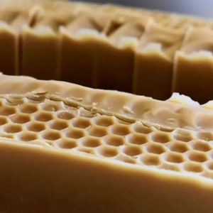 Può includere: Una saponetta al miele con un design a nido d'ape. Il sapone è di colore marrone chiaro e ha una consistenza liscia.