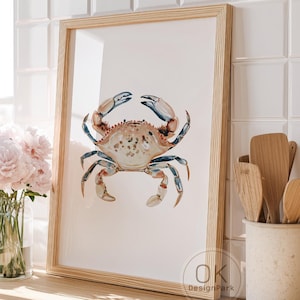 May include: A framed watercolor print of a crab with blue and tan tones. The print is in a light wood frame and is displayed on a kitchen counter. The image also shows a toaster, flowers, and kitchen utensils.