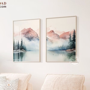 Könnte beinhalten: Zwei Aquarellbilder mit einer Bergseenlandschaft in Rosa- und Blautönen. Die Bilder sind gerahmt und an einer weißen Wand über einem hellbeigen Sofa aufgehängt.
