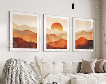 May include: Three abstract landscape prints with a sunset and mountains in shades of orange, brown, and beige. The prints are framed and hanging on a white wall above a white sofa.