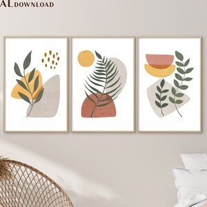 Puede incluir: Tres impresiones de arte abstracto con un dise&ntilde;o minimalista que presenta hojas verdes, formas geom&eacute;tricas amarillas y naranjas y un fondo blanco. Las impresiones est&aacute;n enmarcadas en un marco de madera claro.