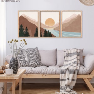 K&ouml;nnte beinhalten: Set aus drei abstrakten Landschaftsdrucken im minimalistischen Stil. Die Drucke zeigen Berge, einen See und einen Sonnenuntergang in gedeckten T&ouml;nen von Braun, Blau und Beige. Die Drucke sind in einem hellen Holzrahmen gerahmt.