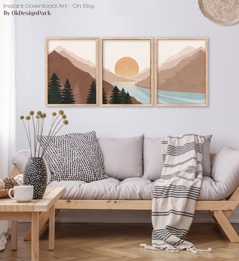K&ouml;nnte beinhalten: Set aus drei abstrakten Landschaftsdrucken im minimalistischen Stil. Die Drucke zeigen Berge, einen See und einen Sonnenuntergang in gedeckten T&ouml;nen von Braun, Blau und Beige. Die Drucke sind in einem hellen Holzrahmen gerahmt.