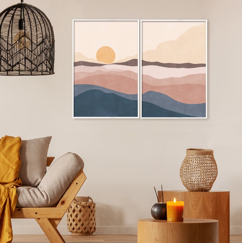 May include: Two framed abstract landscape art prints. The artwork features a warm color palette with a large yellow sun, and layers of blue, brown, and peach tones. The prints are displayed in a modern living room setting.