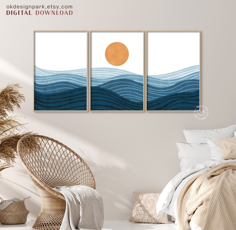 May include: Three framed art prints featuring an abstract ocean wave design in shades of blue, with an orange sun in the center print. The text "okdesignpark.etsy.com DIGITAL DOWNLOAD" is at the top. The artwork is displayed above a wicker chair and bed.