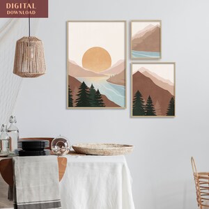 K&ouml;nnte beinhalten: Drei abstrakte Landschaftsdrucke im minimalistischen Stil. Die Drucke zeigen Berge, einen See und eine Sonne in Braun-, Blau- und Wei&szlig;t&ouml;nen. Die Drucke sind in einem hellen Holzrahmen gerahmt.