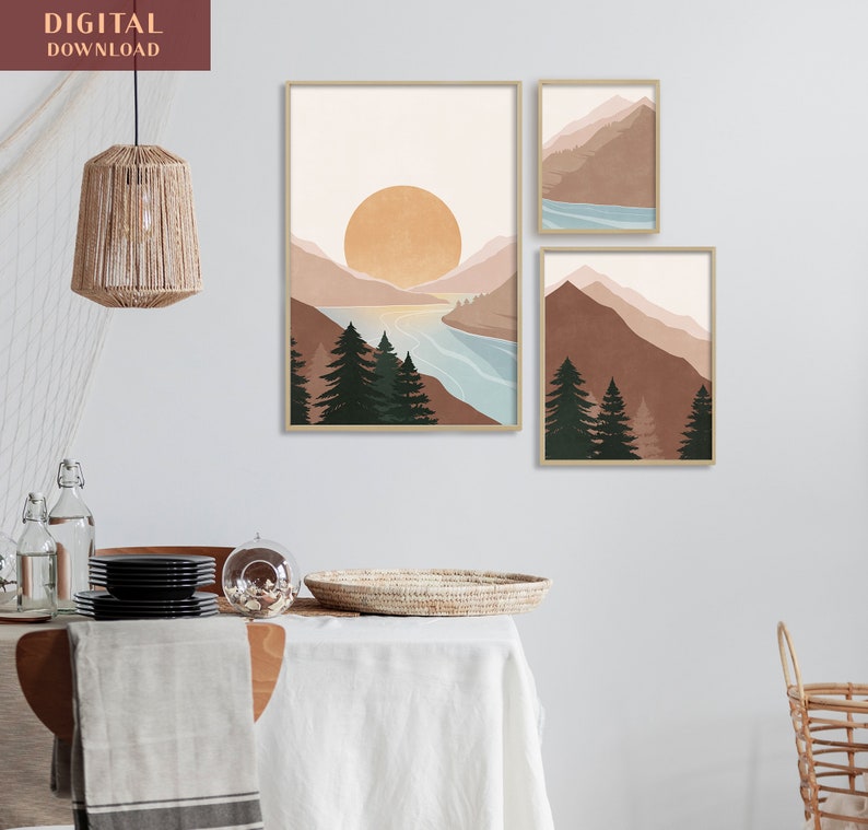 K&ouml;nnte beinhalten: Drei abstrakte Landschaftsdrucke im minimalistischen Stil. Die Drucke zeigen Berge, einen See und eine Sonne in Braun-, Blau- und Wei&szlig;t&ouml;nen. Die Drucke sind in einem hellen Holzrahmen gerahmt.