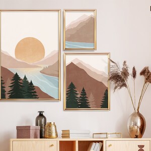 K&ouml;nnte beinhalten: Drei digitale Drucke von abstrakten Landschaften mit Bergen, B&auml;umen und einem See. Die Drucke sind in Gold gerahmt und haben einen minimalistischen Stil.