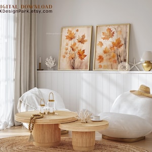 May include: Two framed watercolor paintings of autumn leaves in shades of orange and brown. The paintings are hanging on a white wall above a white couch and a wooden coffee table. The text "OKDesignPark.etsy.com" is visible in the top left corner of the image.