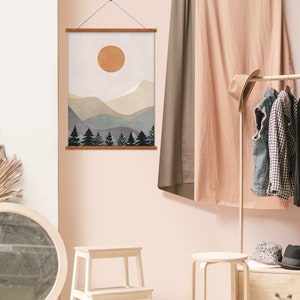 K&ouml;nnte beinhalten: Ein digitaler Download eines minimalistischen Berglandschaftsdrucks mit einer Sonne und B&auml;umen in Braun-, Beige- und Blaut&ouml;nen. Der Druck ist mit einem Holzrahmen gerahmt und an einer Wand aufgeh&auml;ngt.
