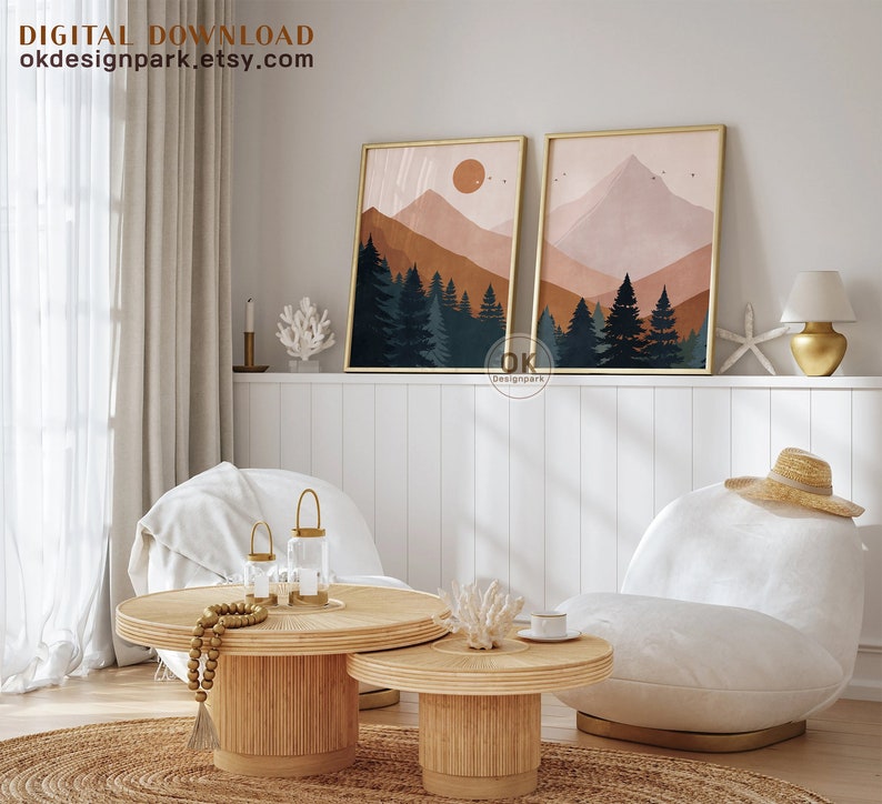 May include: Two abstract landscape prints with a mountain range, trees, and a sun in the sky. The prints are in a gold frame and are hanging on a white wall. The prints are above a white couch with a straw hat on it.
